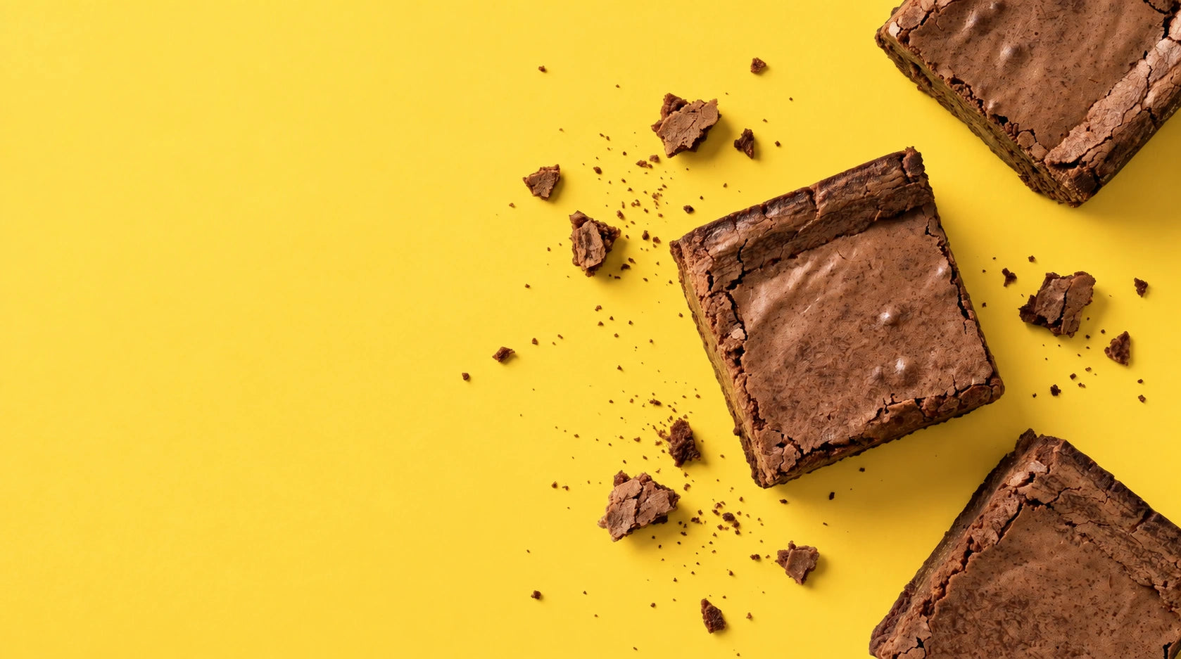 Miles of Chocolate brownies with crisp chocolate tops and scattered crumbs on a yellow background
